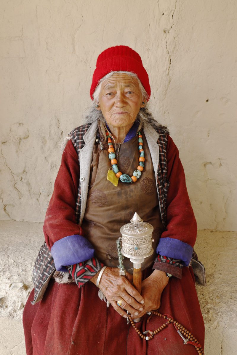 En kvinna från Ladakh vid Lamayuru klostret med bönekvarn och mala i handen.